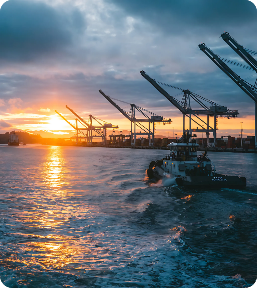 A tugboat navigating a harbor at sunset, with shipping cranes in the background, symbolizing marine emission control and cleaner fuel solutions.