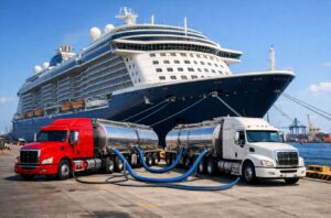 Red and white bulk tanker trucks delivering 30,000 liters of AUS40 marine urea to a Royal Caribbean cruise ship at berth to meet IMO Tier III emission compliance